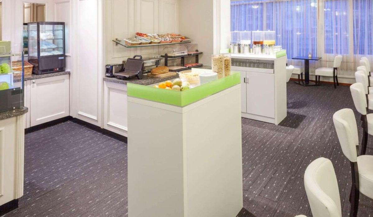 ibis Styles Amsterdam City - La sala colazioni è arredata con tavoli in legno chiaro, sedie moderne dai colori vivaci e lampade sospese. Le grandi finestre rendono l’ambiente luminoso e piacevole.
