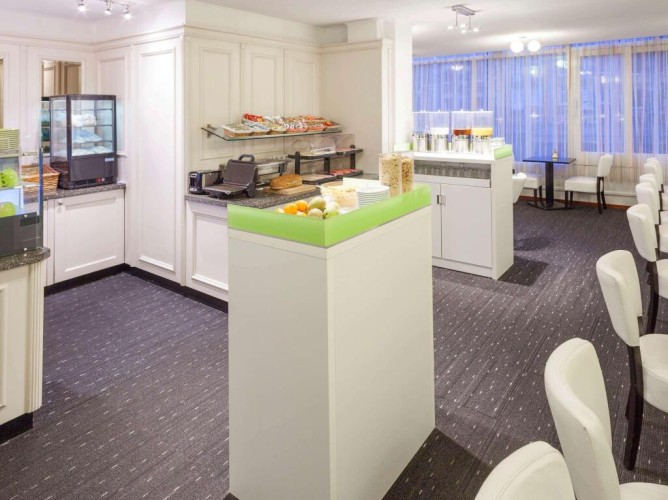 ibis Styles Amsterdam City - La sala colazioni è arredata con tavoli in legno chiaro, sedie moderne dai colori vivaci e lampade sospese. Le grandi finestre rendono l’ambiente luminoso e piacevole.