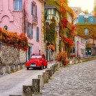 Una strada accogliente di Montmartre, con foglie autunnali che tappezzano i vicoli acciottolati. Una classica auto rossa Diane spicca sullo sfondo pittoresco del quartiere parigino.