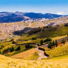 Paesaggio andino pittoresco in Ecuador, tra il Canyon di Zumbahua e la Laguna Quilotoa, con una strada sterrata che attraversa campi coltivati e scenari montani.