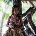 Una giovane ragazza indigena Wayuri, vestita con l’abito tradizionale appoggiata a un albero nella giungla amazzonica ecuadoriana.