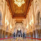 Gli interni della Moschea di Hassan II sorprendono per la navata maestosa, decorata con intarsi di legno, stucchi raffinati e lampadari di cristallo che diffondono luce calda e avvolgente.