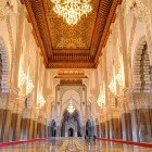 Gli interni della Moschea di Hassan II sorprendono per la navata maestosa, decorata con intarsi di legno, stucchi raffinati e lampadari di cristallo che diffondono luce calda e avvolgente.