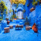 Un cortile tipico nella medina blu di Chefchaouen, con pentole di terracotta, tavolino e sedie rustiche, trasmette calore e autenticità nella tradizione marocchina.