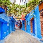 Un vicolo pittoresco e blu di Chefchaouen si snoda tra pareti dipinte e negozietti nascosti, dove l’arte locale e la vita quotidiana si fondono in un’atmosfera autentica e magica.