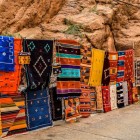 Nel souk di Tinghir, i tappeti berberi tessuti a mano raccontano storie di tradizione e maestria artigianale, esposti sotto il cielo del deserto.