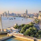 Vista panoramica di Shanghai con il fiume Huangpu che attraversa la città, grattacieli moderni e luci spettacolari che riflettono sull’acqua.