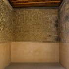 Interno di Mitla con pareti ornate da intricati mosaici geometrici zapotechi, intonaco ocra e pietre antiche, sotto un soffitto in legno che dona autenticità all’ambiente cerimoniale.