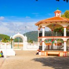 La piazza di Zinacantán, davanti alla chiesa di San Lorenzo, mostra un elegante gazebo bianco e arancione decorato con bandierine colorate, circondato da colline verdi e vita locale autentica.