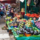 Una donna e una bambina tzotziles al mercato di San Cristóbal espongono frutta fresca su teli verdi e celesti, creando una scena autentica fatta di colori, tradizione e vita quotidiana indigena.
