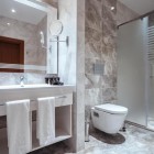 Bagno moderno ed elegante con doccia in vetro, rivestimenti effetto marmo, lavabo ampio e specchio illuminato. Ambiente luminoso, curato e confortevole.