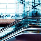 Interni moderni dell’aeroporto di Baku con ampie vetrate, scale mobili eleganti e design futuristico. Spazi luminosi e linee curve creano un’atmosfera raffinata e contemporanea.