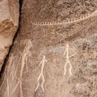 Incisioni rupestri preistoriche su roccia raffigurano figure umane stilizzate e animali. Antiche testimonianze artistiche che raccontano vita, riti e cultura delle civiltà primitive.