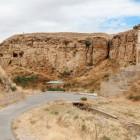 Il Mausoleo di Diri Baba in Azerbaigian, incastonato nella roccia, domina un paesaggio arido con scalinata storica, strada panoramica e colline dal fascino suggestivo.