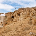 Il Mausoleo di Diri Baba, incastonato nella roccia in Azerbaigian, mostra una cupola bianca, archi in pietra e paesaggio arido con colline e pareti rocciose suggestive.