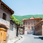 Tipiche case storiche di Sheki, in Azerbaigian, con facciate in pietra e mattoni, balconi in legno e tetti tradizionali, immerse tra verdi colline dell’Alto Caucaso.