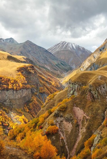 Spettacolare paesaggio autunnale lungo la Strada Militare Georgiana: vallate dorate, canyon profondi e vette del Caucaso avvolte da nuvole, tra silenzi e natura selvaggia.
