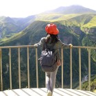 Una viaggiatrice ammira la Valle del Diavolo dal Monumento dell’Amicizia a Gudauri: canyon verdi e montagne del Caucaso si aprono in un panorama mozzafiato.