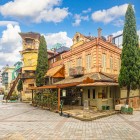 Nel quartiere antico di Tbilisi, case in legno, balconi scolpiti e una torre con orologio creano un’atmosfera fiabesca tra vicoli acciottolati e caffè storici.