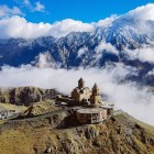 La Chiesa della Trinità di Gergeti emerge tra le nuvole ai piedi del Monte Kazbek, sospesa sui paesaggi del Grande Caucaso e circondata da vette maestose e silenzio alpino.