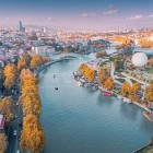 Vista aerea di Tbilisi, con il fiume Mtkvari (Kura) che attraversa la città, il Ponte della Pace e i parchi lungo il lungofiume tra architettura storica e moderna.