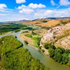 Veduta aerea della città rupestre di Uplistsikhe, antico insediamento scavato nella roccia che domina il fiume Mtkvari, circondato da colline e paesaggi spettacolari della Georgia.