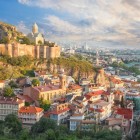 Panorama della città vecchia di Tbilisi, con la fortezza di Narikala che domina le case colorate e il fiume Mtkvari, tra storia millenaria e architettura moderna.