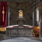 Interno del monastero di Khor Virap con altare in pietra, icone sacre e luci soffuse che creano un’atmosfera raccolta e spirituale, tipica dell’architettura armena.
