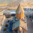 Il monastero di Khor Virap, in stile armeno, presenta pietra tufacea, pianta compatta e cupola conica. Linee essenziali e armoniose nel paesaggio.