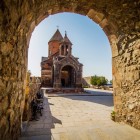 Vista del monastero di Khor Virap attraverso un arco in pietra, con linee armoniose e dettagli tipici illuminati dalla calda luce dell’Armenia.