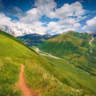 Sentiero tra le colline verdi della Svaneti con vista sulle vette del Caucaso. Un paesaggio incontaminato ideale per trekking tra natura e panorami spettacolari.