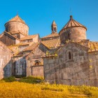 Veduta del Monastero di Haghpat, in Armenia, con chiese in pietra e cupole coniche illuminate dalla luce dorata, tra dettagli medievali e atmosfera suggestiva.