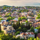 Splendido paesaggio mattutino del centro storico di Kutaisi, in Georgia, con la cattedrale cattolica in primo piano tra alberi verdi e le montagne sullo sfondo.
