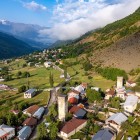 Veduta aerea di Mestia, nel cuore della Svaneti, con torri medievali in pietra tra prati verdi e paesaggi alpini, dominati dalle maestose vette del Caucaso.