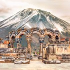 Antiche rovine della Cattedrale di Zvartnots in Armenia, con eleganti archi in pietra scolpita sullo sfondo del maestoso Monte Ararat innevato.