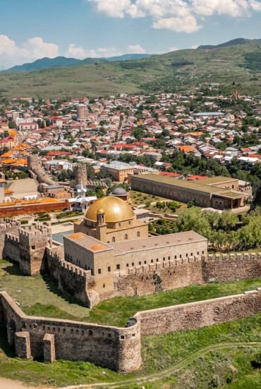Vista panoramica di Akhaltsikhe con la fortezza di Rabati, mura medievali, torri e cupole dorate, immersa tra colline verdi e il paesaggio autentico della Georgia.