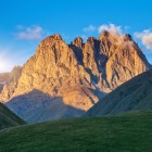 Le maestose vette del Monte Chaukhebi si tingono di luce dorata al tramonto, dominando vallate alpine e scenari spettacolari nel Parco Nazionale di Kazbegi.