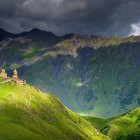 La Chiesa della Trinità di Gergeti domina le colline di Kazbegi, sospesa tra prati verdi e le grandi pareti del Caucaso che chiudono l’orizzonte.