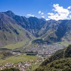 Veduta di Stepantsminda adagiata nella valle ai piedi delle montagne del Caucaso, circondata dalle grandi vette che dominano il paesaggio del Kazbegi.