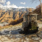 Antica fontana in pietra nei pressi della Chiesa di Gergeti, con acqua di sorgente che scorre tra i monti del Caucaso e panorami aperti sulla valle di Kazbegi.