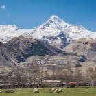 Veduta del villaggio di Gergeti ai piedi del Monte Kazbek, con le case raccolte nella valle e le cime innevate del Grande Caucaso a dominare l’orizzonte.