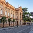 Palazzo storico su Empty Street a Kutaisi, con facciata in stile classico, archi eleganti e decorazioni raffinate. Un esempio armonioso dell’architettura urbana locale.