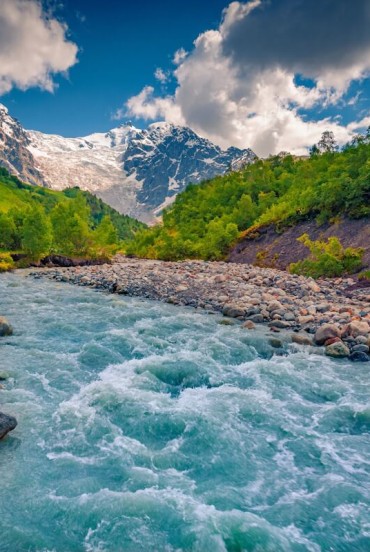 Le acque azzurre del fiume Adishchala scorrono lente ai piedi del monte Shkhara, regalando al mattino una luce limpida sull’Alta Svaneti e sul villaggio di Adishi.