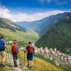 Discesa a piedi verso Iprali tra prati e sentieri di montagna. Le torri svane emergono tra le case, mentre la valle si apre lenta tra boschi e silenzi.