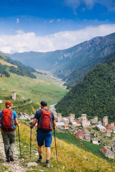 Discesa a piedi verso Iprali tra prati e sentieri di montagna. Le torri svane emergono tra le case, mentre la valle si apre lenta tra boschi e silenzi.