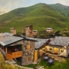 Guesthouse in pietra tra le colline dello Svaneti, con luci calde e torri medievali sullo sfondo. Un luogo semplice e autentico dove la sera scorre lenta tra natura.