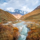 Il fiume Enguri, dalle acque lattiginose, attraversa una valle dorata nello Svaneti. Scorre tra silenzi e pendii morbidi, con le vette del Caucaso a fare da sfondo.