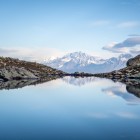 Lago Udziro tra rocce d’alta quota riflette le vette innevate del Caucaso. Acque calme e cielo limpido accompagnano un paesaggio essenziale e silenzioso.