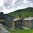 Tipica guesthouse in pietra nello Svaneti, tra prati verdi e montagne del Caucaso. Atmosfera autentica, luci calde al tramonto e silenzi che raccontano la vita di montagna.
