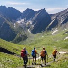 Escursionisti lungo un sentiero nel Grande Caucaso, tra vallate verdi e creste rocciose. Il percorso scende tra silenzi aperti e neve residua che accompagna il cammino.
